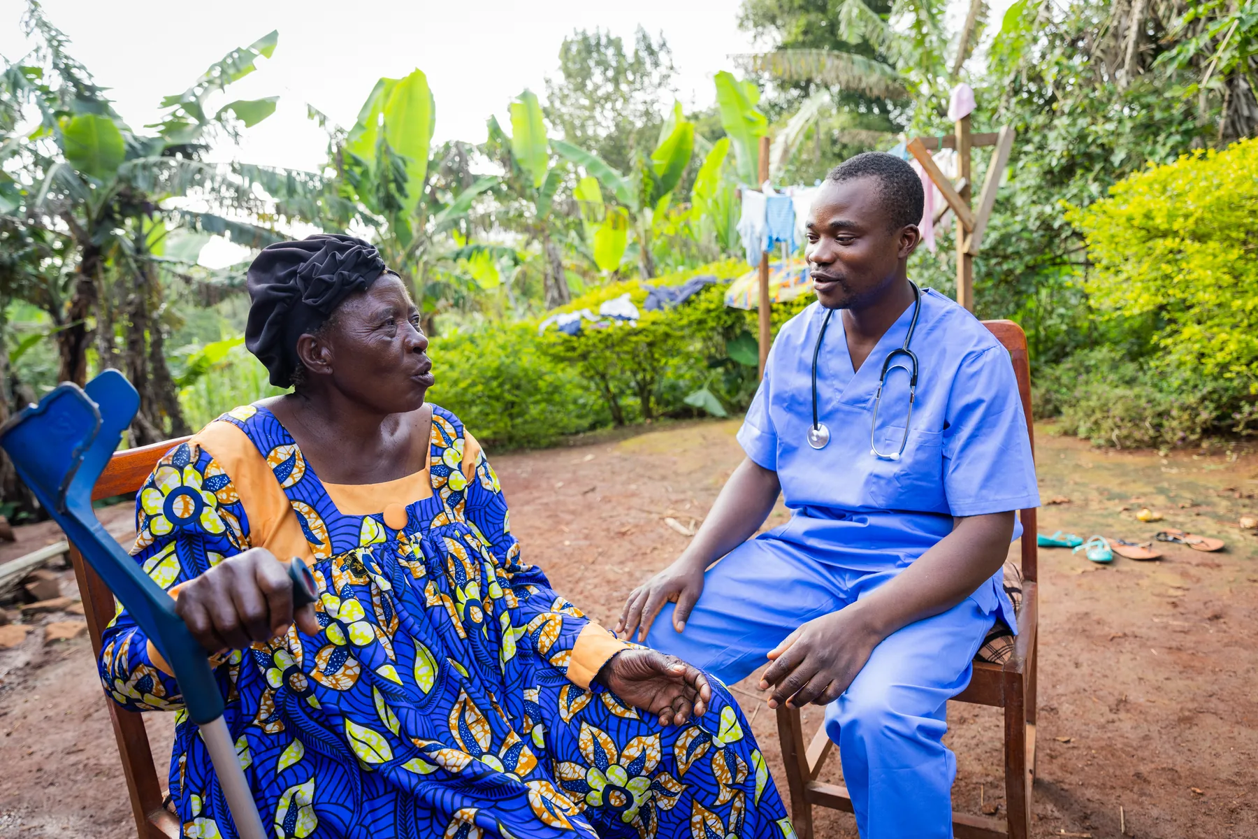 A man in blue scrubs talking with an older woman outdoors.